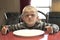 A Upset little boy waiting for dinner while holding a fork and a spoon