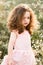 Upset little girl with curls walks in chamomile field