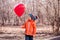 Upset little toddler child in orange jacket standing with unhappy face expression looking at big red heart-shaped balloon