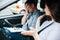 Upset male driving examiner in gray shirt and jeans makes facepalm gesture with one hand and holds clipboard with