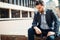 An upset man in a suit sits on a curb with his head bowed side view