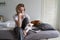 Upset mature woman with pay bills and calculator sits on bed with dog in home m interior