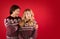 Upset millennial girl in Christmas outfit and boyfriend comforting her on red background, free space