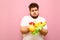 Upset overweight boy holds apples, tangerine, orange, banana and lettuce in hands and looks at the fruit in his sad face. Fat