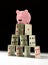 Upset piggy bank standing on fragile shaky house of cards with a dark background