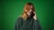 Upset Red haired Caucasian Woman Talking on Phone on Green Background
