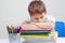 Upset schoolboy sitting at desk with pile of school books and notebooks