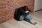 Upset teenage girl with backpack sitting on floor near wall.