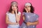 Upset and tired women standing against pink studio wall with exhausted facial expressions after having fun together, posing in