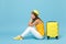 Upset tourist woman in summer casual clothes sit on suitcase put hands on head isolated on yellow orange background