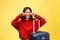 Upset tourist woman in summer casual clothes sit on suitcase put hands on head on yellow orange background