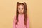 Upset unhappy little girl with ponytails wearing pink sweatshirt isolated over beige background looking at camera with pout lips