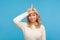 Upset unlucky woman with curly blond hair showing looser gesture holding finger near forehead, depressed with her fail