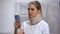 Upset woman in foam cervical collar reading bad news in smartphone, trauma