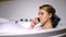 Upset woman talking phone in bath with foam bubbles, negative news, close-up