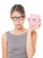 Upset woman wearing glasses holding piggy bank