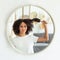 Upset young attractive african american lady pulls out comb from curly hair, looks in reflection of round mirror