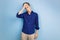 Upset young man in blue shirt, holding hand on forehead, forgetting something or feeling sadness, standing over blue