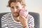 Upset young man with piggy bank at home