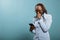 Upset young woman crying after reading tragic news on smartphone device while standing on blue background.