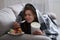 Upset young woman dealing with depression by eating ice cream and sweets under blanket on sofa