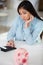 Upset young woman with empty piggy bank at home