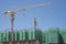 Upward view of precast building cover by green net, large tall Tower Crane moving machine in construction work, under blue
