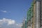 Upward view of precast building cover by green net, large tall Tower Crane moving machine in construction work, under clear blue