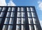 Upwards view of the corner of a black modern office building with blue sky and clouds reflected in large glass windows