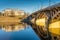 Urban architecture, a bridge in retro style with arched spans and massive yellow supports is reflected in the blue river