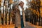 Urban attractive young blonde woman with a stylish hairstyle in a fashionable coat in vintage jeans stands on an alley in the park