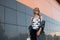 Urban attractive young hipster woman in stylish clothes in vintage sunglasses with a backpack poses in a city near a modern gray