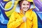 Urban bright portrait cool young woman in hood with cheerful smile wearing in yellow jacket posing against wall painted