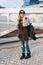 Urban fashionable young woman in cool sunglasses, warm winter sweater, stylish jeans travelling with backpack in city