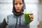 Urban fitness woman showing detox smoothie cup on workout rest