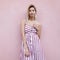 Urban happy stylish young woman blonde with cute smile in vintage striped long dress posing near a pink building on the street