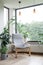 Urban jungle apartment. Grey armchair near big panoramic window, indoor plants, monstera, palm trees. Biophilia design