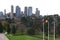 Urban park with trees, grass, flagpoles and iconic cityscape of modern skyscrapers in Melbourne downtown, Victoria, Australia