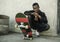 Urban portrait of young attractive and serious black afro American man with skate board squatting on street corner looking cool
