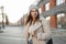 Urban pretty stylish young woman in a vintage hat in a trendy coat with a fashion black leather handbag standing in a parking lot