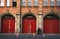 Urban symmetry in London. People passing by an industrial building with big red doors