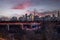 An urban waterfront town skyline with illuminated high-rise buildings under a sunset cloudscape