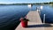 US flags and red flowers in pot on a boat dock while a pontoon on a beautiful Minnesota lake passes by on July 4th.