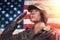 USA celebration. Portrait of a female soldier saluting, against the background of the American flag. Side view. Light