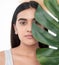 Use nature to nurture your skin. a beautiful young woman holding a palm frond against her face.