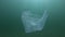 Used blue plastic bag slowly drifts underwater in sun rays. Plastic garbage environmental pollution problem. Plastic debris