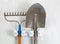 Used garden tools hanging from rack on white wooden boards