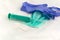 Used green disposable face mask, blue latex glove and plastic syringe lying on a white table. Typical surgical mask to cover the