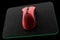 Used metal red gaming mouse with scratches on professional pad isolated on black