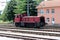 Used old dark red electric locomotive waiting for departure in front of new railway station building